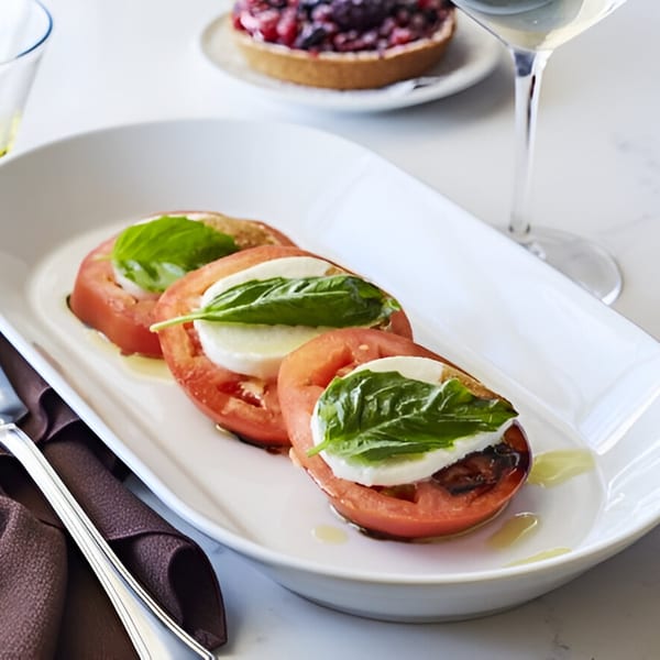 Caprese salad with sliced tomatoes, mozzarella, basil, and balsamic glaze on a white plate.