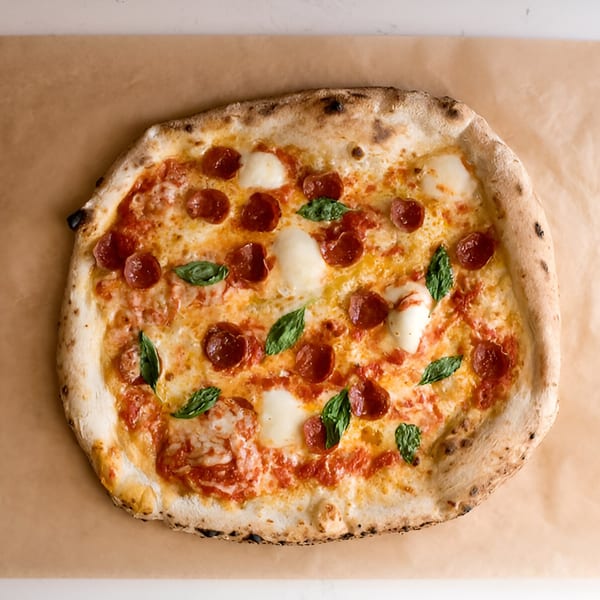 Napoli 1 Pizza's pepperoni pizza with fresh mozzarella and basil on a brown paper background.